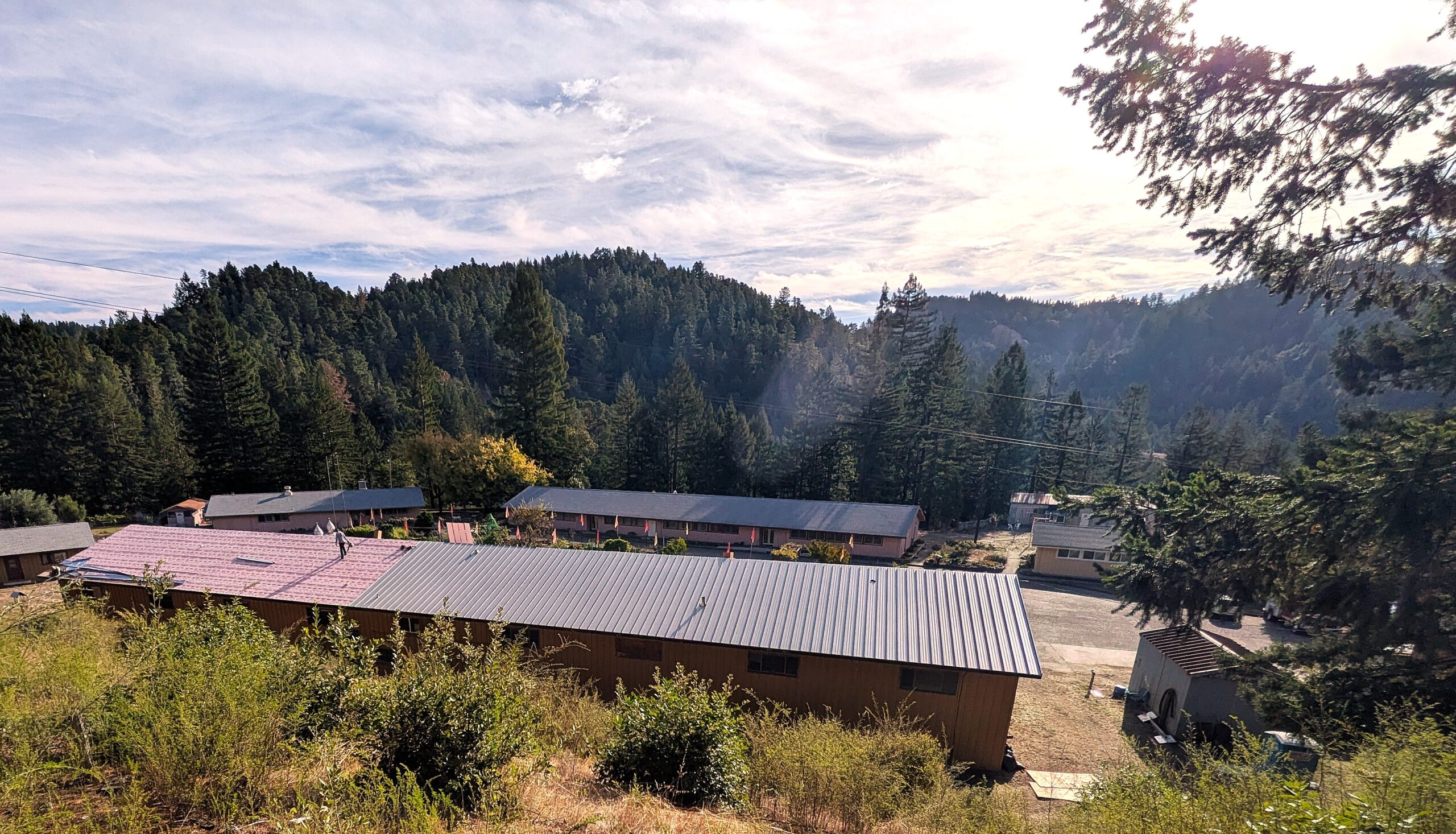 Photo taken from above showing half of the building's new metal roof in place, with underlayers in place for the other half. The new roof panels are long, light-colored, standing seam.